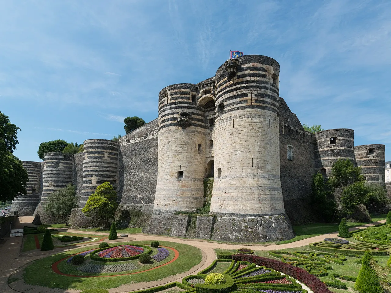 Le château d’Angers et ses tours rayées de schiste sombre et de tuffeau clair, dominant des parterres fleuris et des haies de buis taillées.