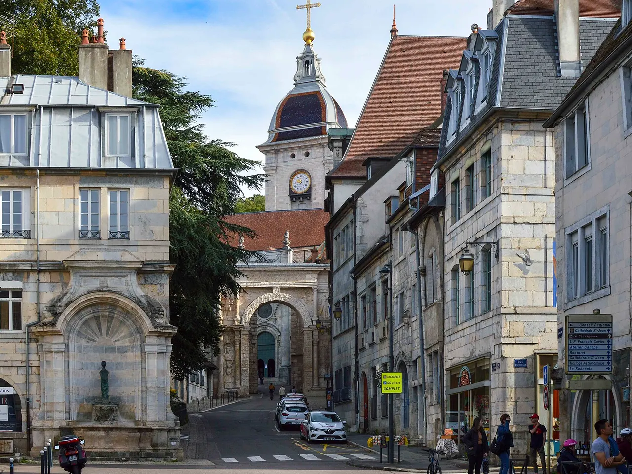 Rue de Besançon en pierre claire menant à la Porte Noire romaine, avec le clocher à dôme de la cathédrale Saint-Jean au-dessus