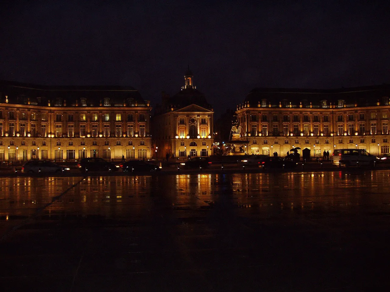 La place de la Bourse à Bordeaux illuminée la nuit, ses façades dorées se reflétant sur le miroir d’eau.