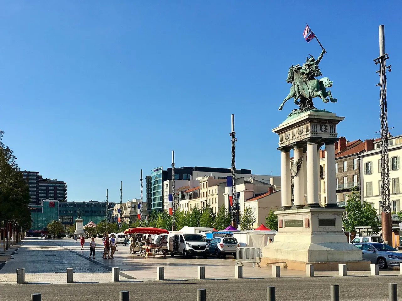 La place de Jaude à Clermont-Ferrand, la statue équestre de Vercingétorix brandissant un drapeau et des étals de marché sous un ciel bleu.