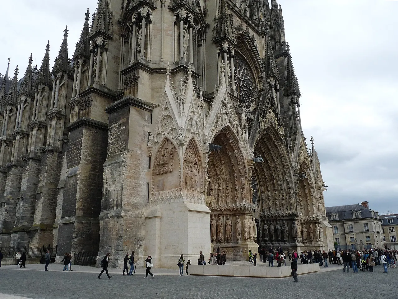 Les portails sculptés de la façade de la cathédrale Notre-Dame de Reims, avec des visiteurs sur le parvis.