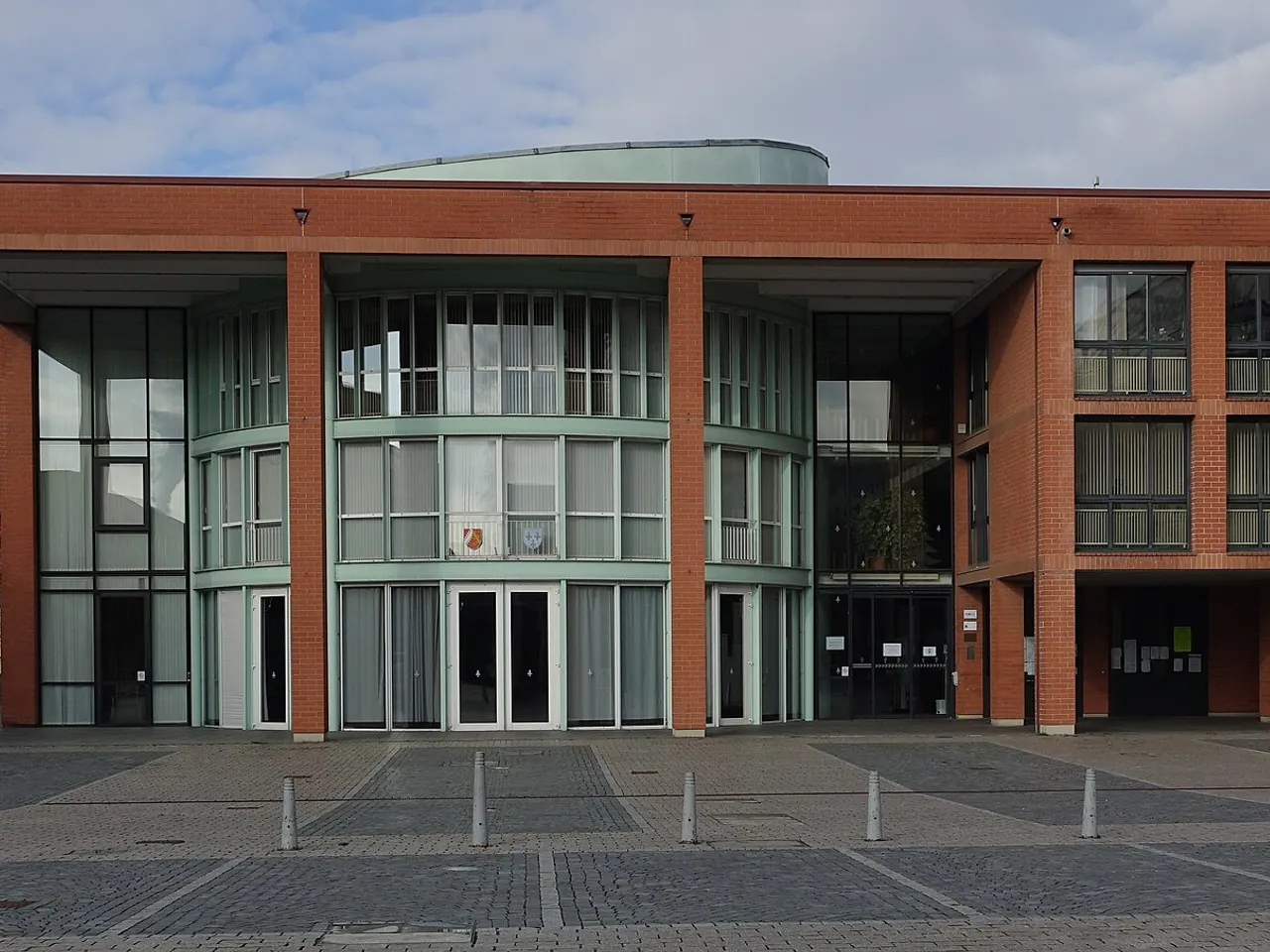 La façade de brique rouge et de verre de l’hôtel de ville de Saint-Louis, ornée de deux blasons, sur une place pavée